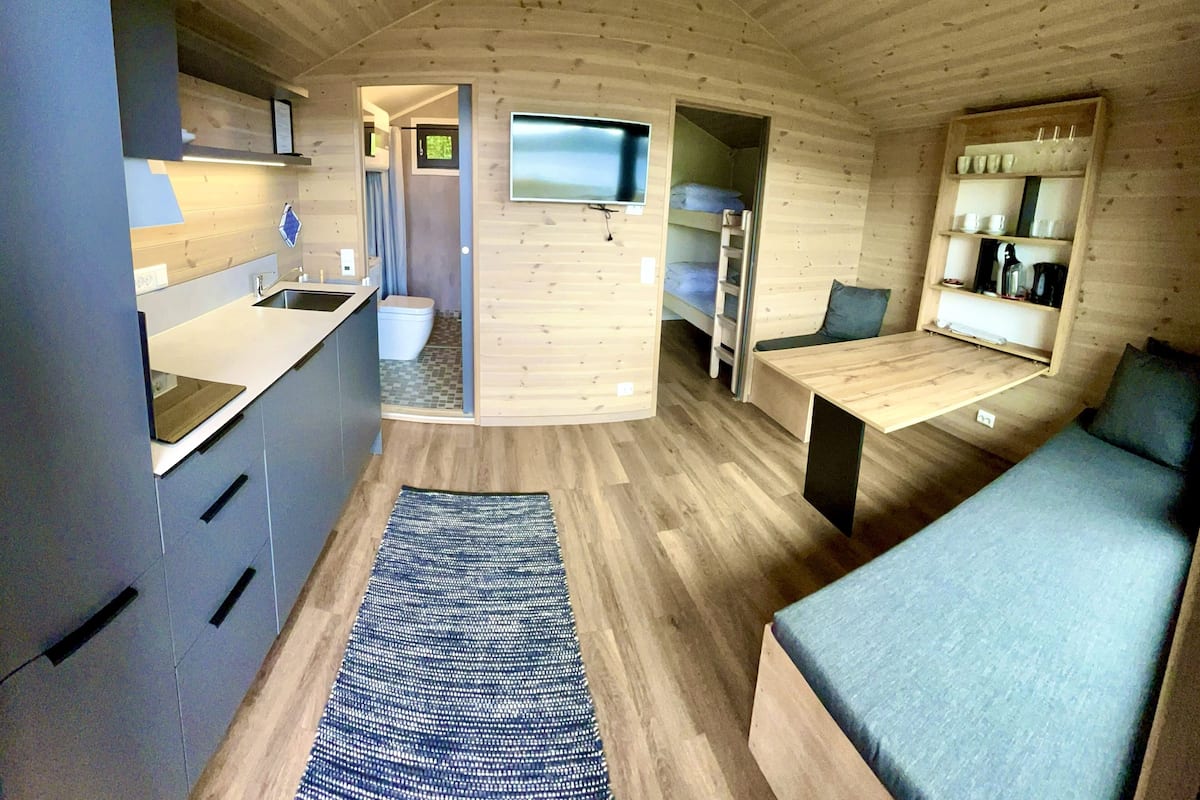 Une petite cabane moderne comprenant un coin cuisine, un espace repas et un espace nuit.