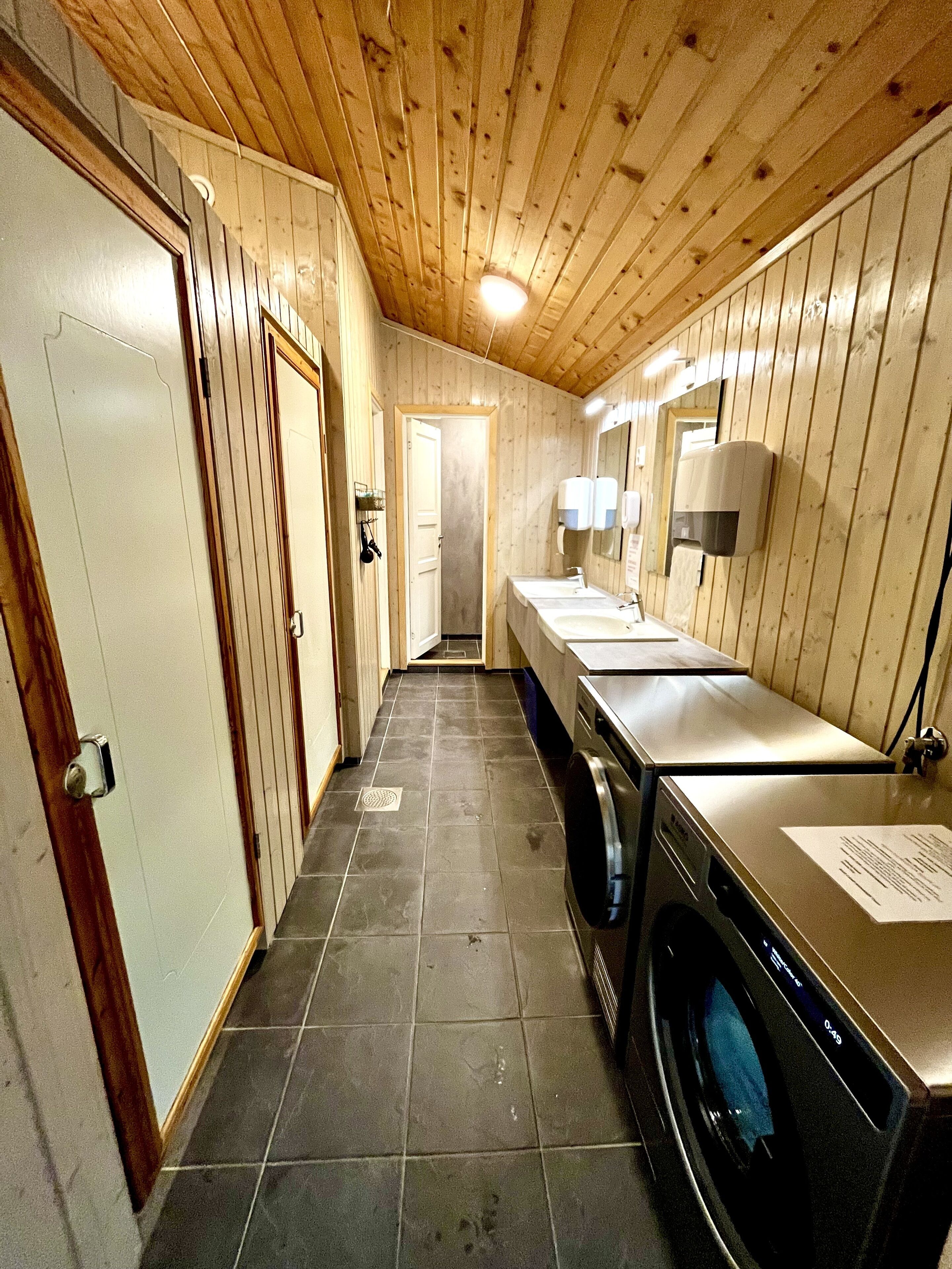 A narrow hallway with wooden walls and a tiled floor leading to a bathroom with a washing machine and a sink.
