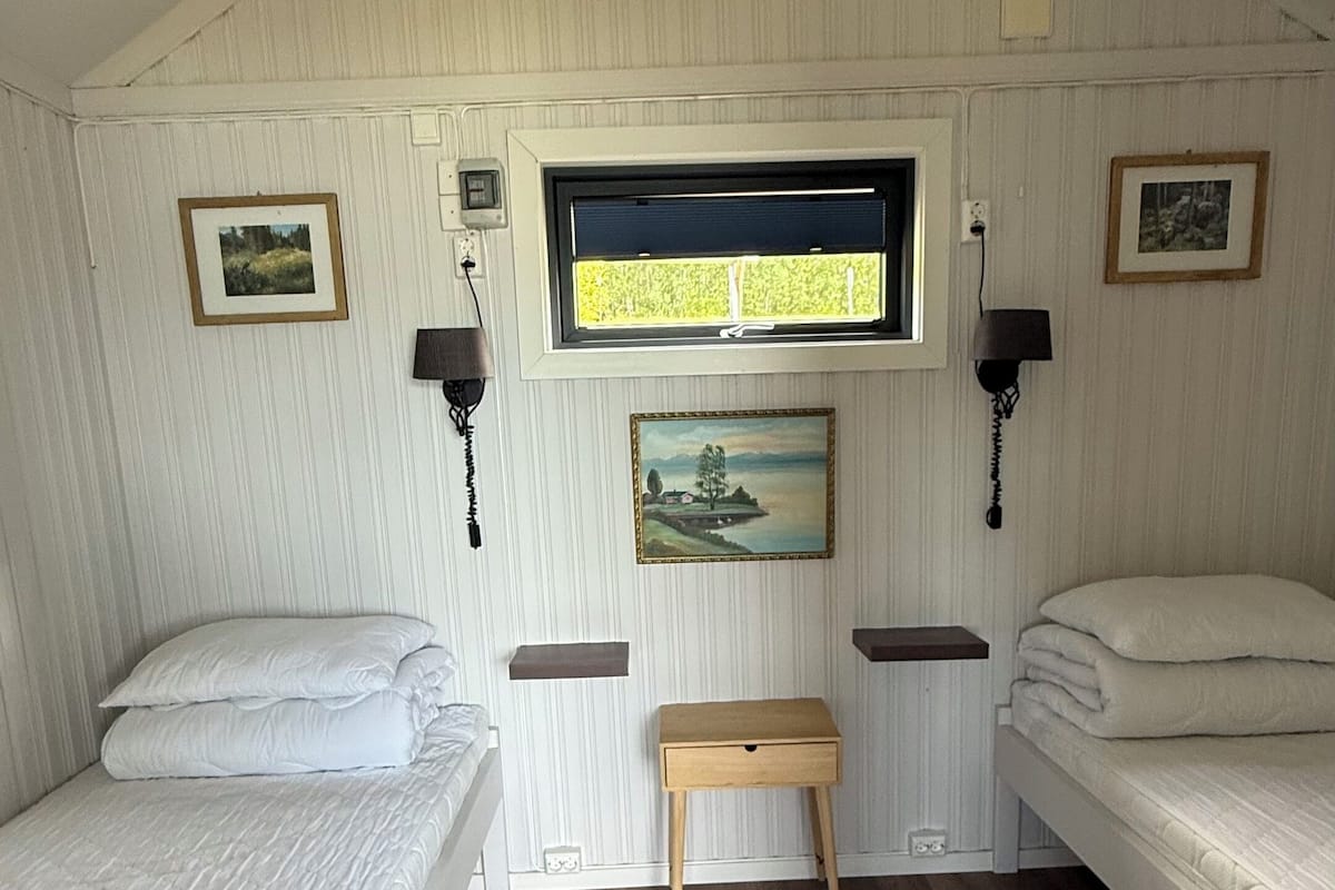 Une chambre avec deux lits, un banc en bois et une fenêtre donnant sur des arbres.