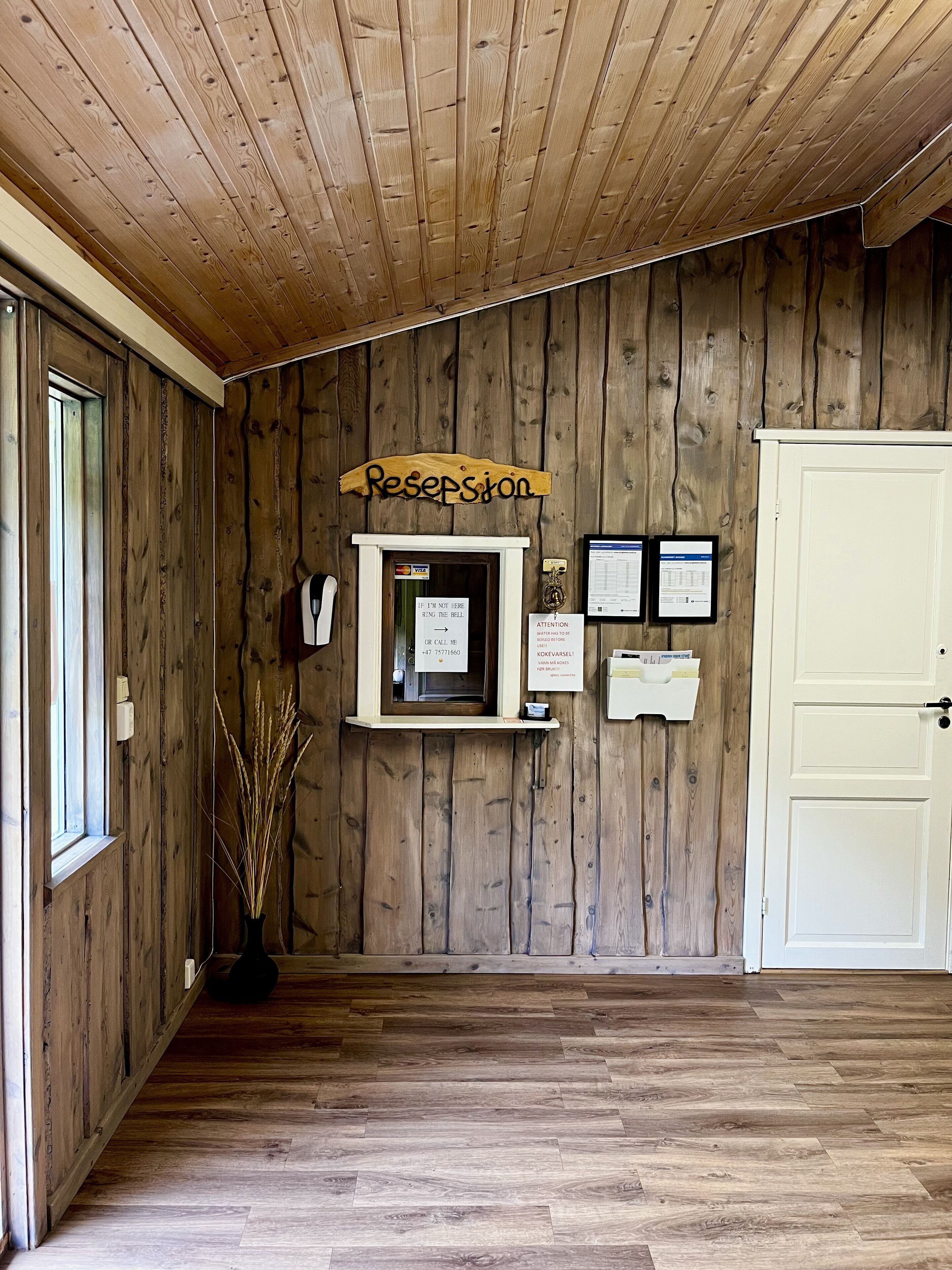 A reception area with a wooden wall, a reception desk, a sign reading "Reception", and a door to the right.
