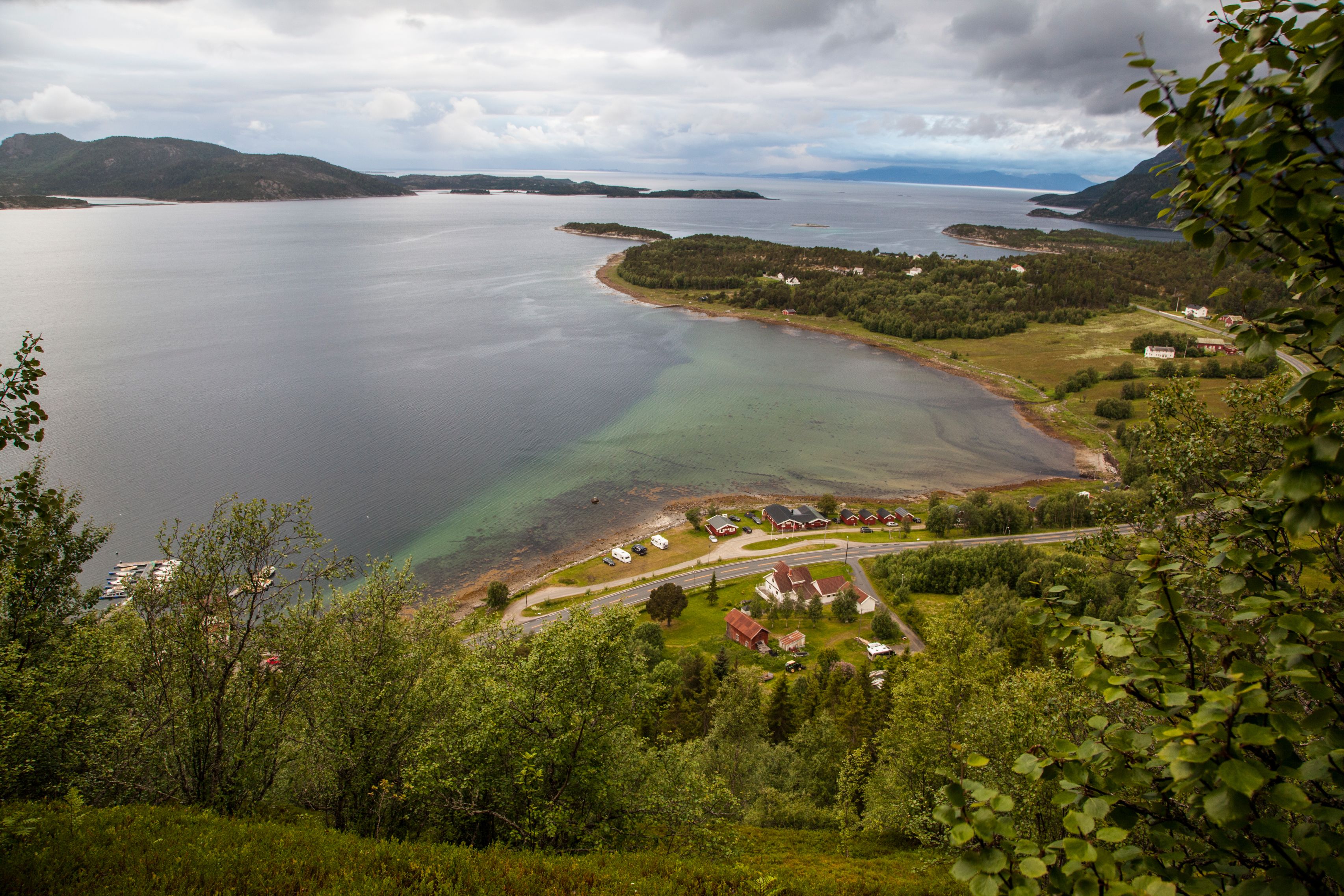 A coastal landscape with a road leading to a cluster of houses near the water.
