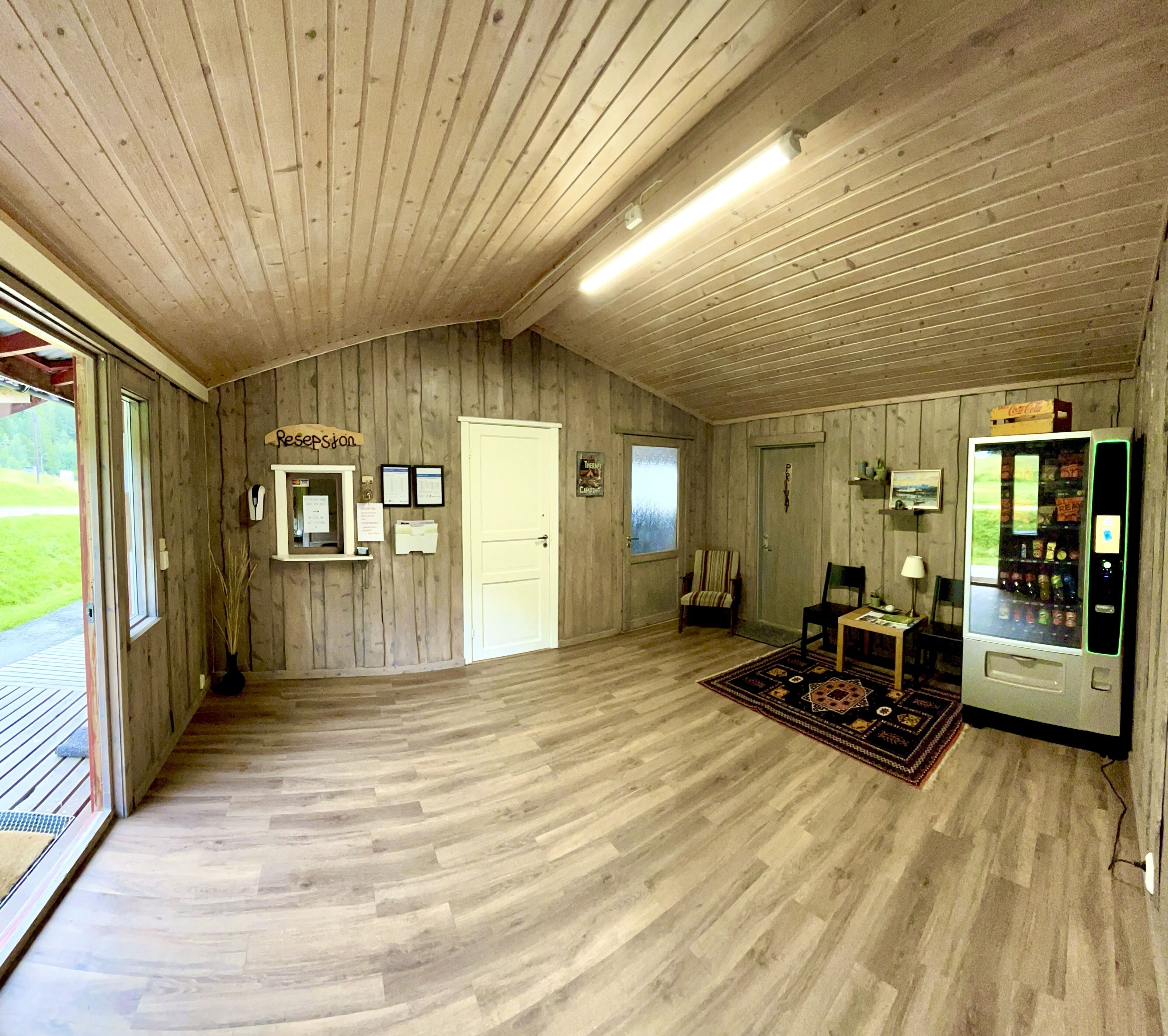 A reception area with a wooden interior, a reception desk, a door, a window, and a vending machine.