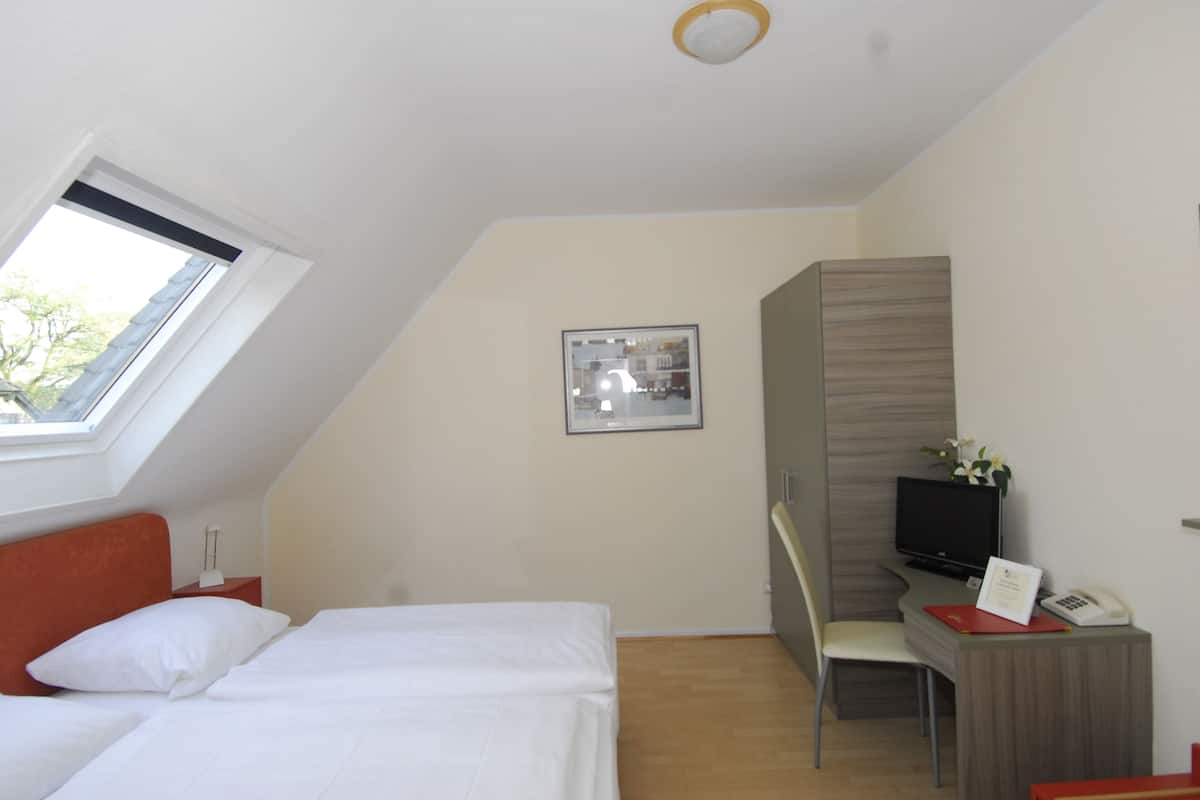 Ein Schlafzimmer mit Bett, Schreibtisch, Stuhl, Fernseher und Fenster.