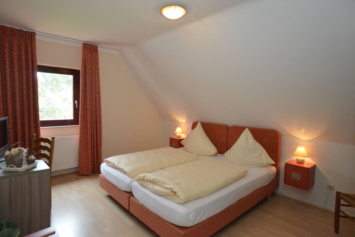 Ein Schlafzimmer mit einem Bett, zwei Nachttischlampen, einem Schminktisch und einem Fenster mit Vorhängen.