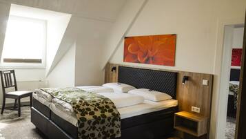 A bedroom with a bed, a chair, a radiator, a wall-mounted light, and a painting.