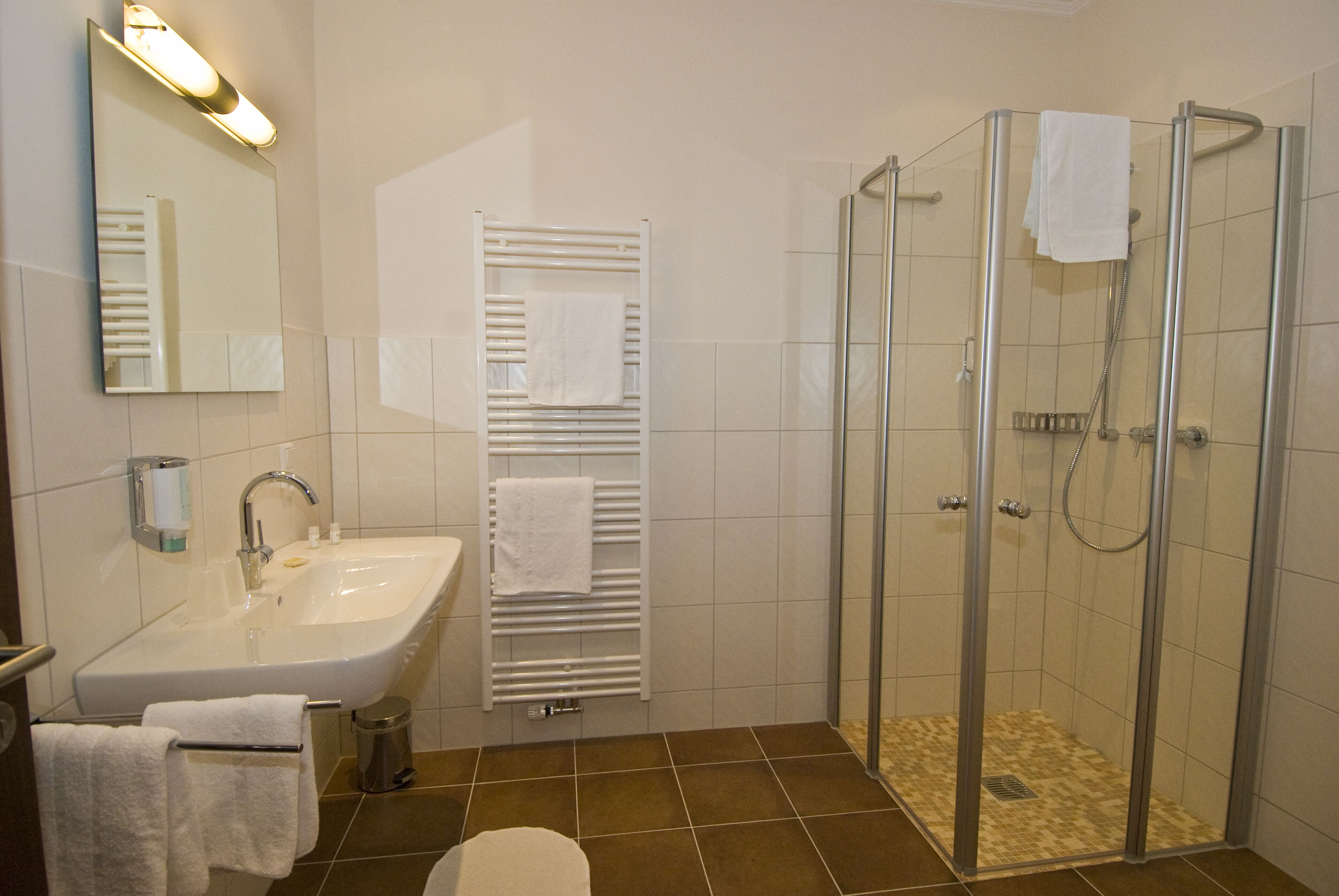 A bathroom with a sink, mirror, towel rack, and a glass-enclosed shower.