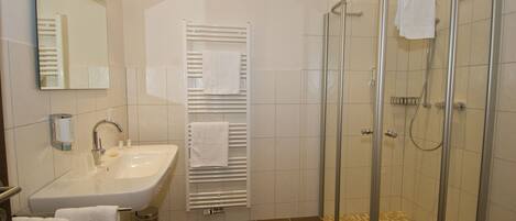A bathroom with a sink, mirror, towel rack, and a glass-enclosed shower.