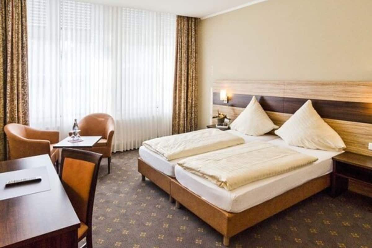 Ein Hotelzimmer mit Doppelbett, Schreibtisch mit Stuhl, einem kleinen Tisch und einem Fenster mit Vorhängen.