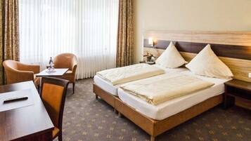Une chambre d’hôtel avec un lit double, un bureau avec une chaise, une petite table et une fenêtre avec des rideaux.