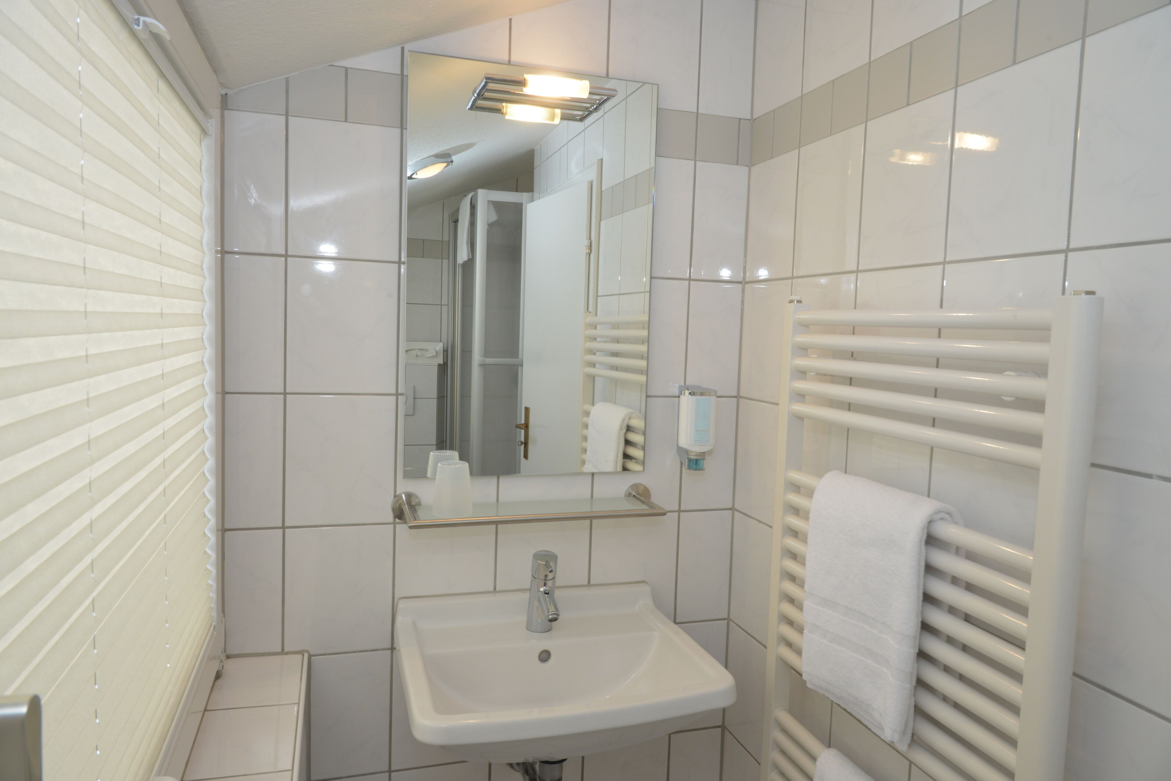 Un baño con un lavabo blanco, un espejo, un perchero para toallas y una zona de ducha.