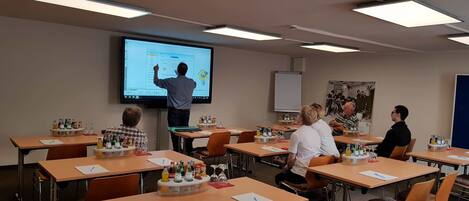 Une salle de classe équipée d’un écran de présentation, de tables avec des bouteilles et d’un projecteur.