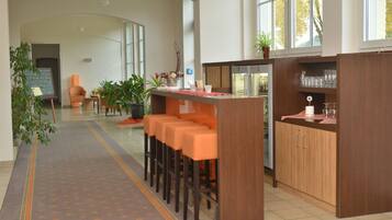 Un moderno vestíbulo de hotel con mostrador de recepción, taburetes de bar, zona de estar con una silla y plantas en macetas.