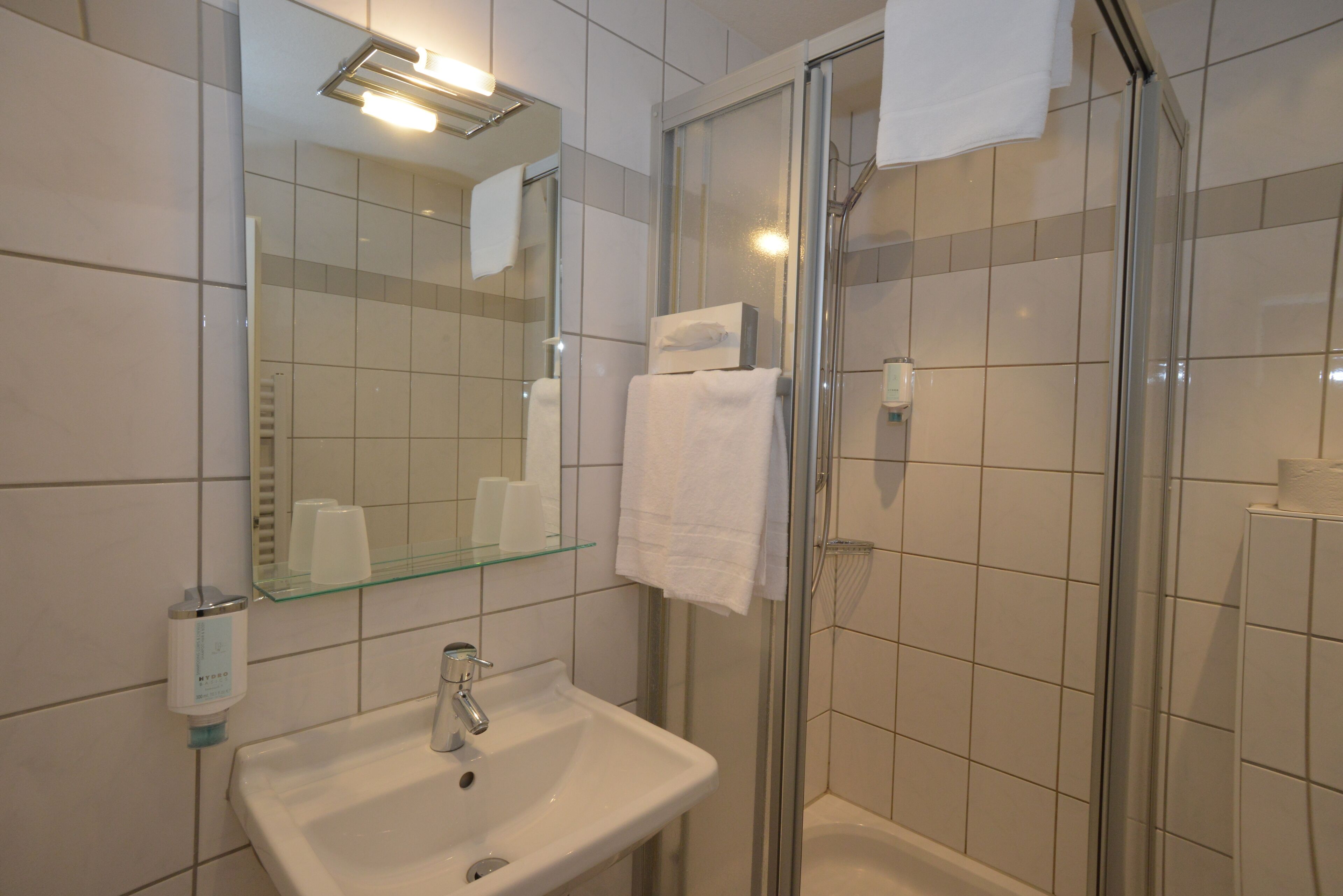 Un baño con cabina de ducha de vidrio, un lavabo con espejo y una repisa de vidrio con artículos de aseo.