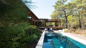A modern outdoor pool area with a wooden deck, lounge chairs, and a pergola. - Pestana Tróia (Grandola)