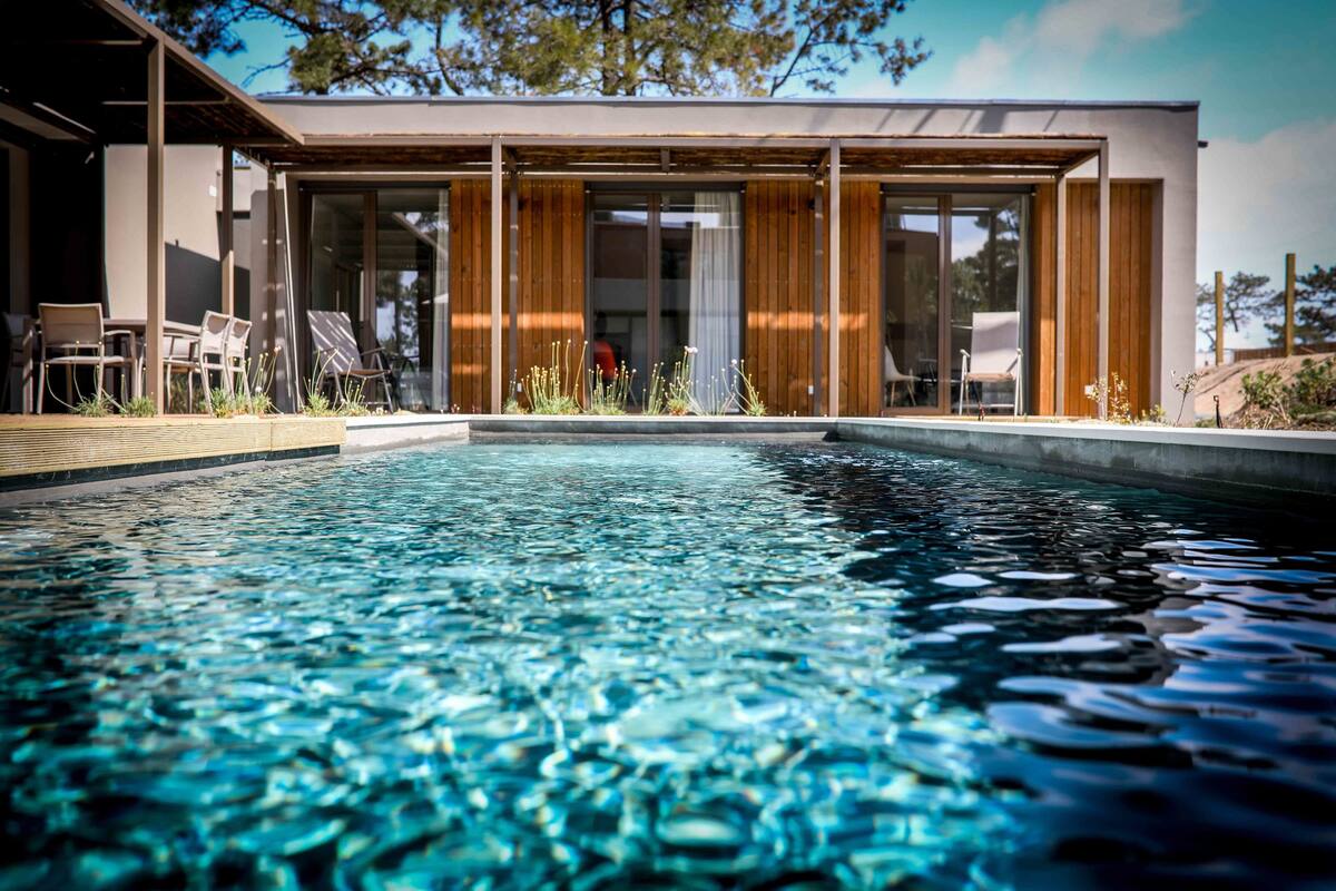 Una casa moderna con piscina, terraza de madera y puertas de cristal que dan a un patio.