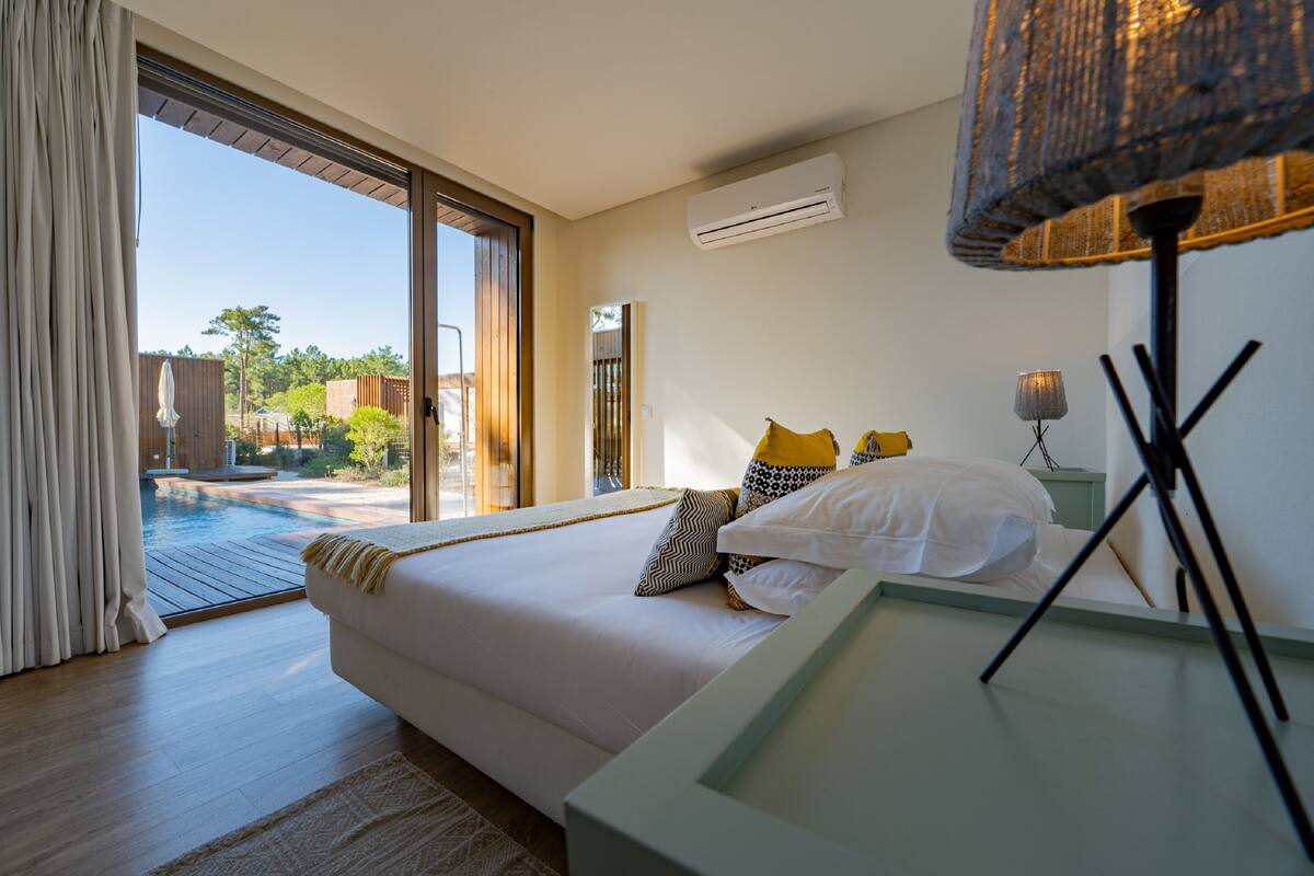 Un dormitorio con una cama grande, vistas a una piscina y un equipo de aire acondicionado en la pared.
