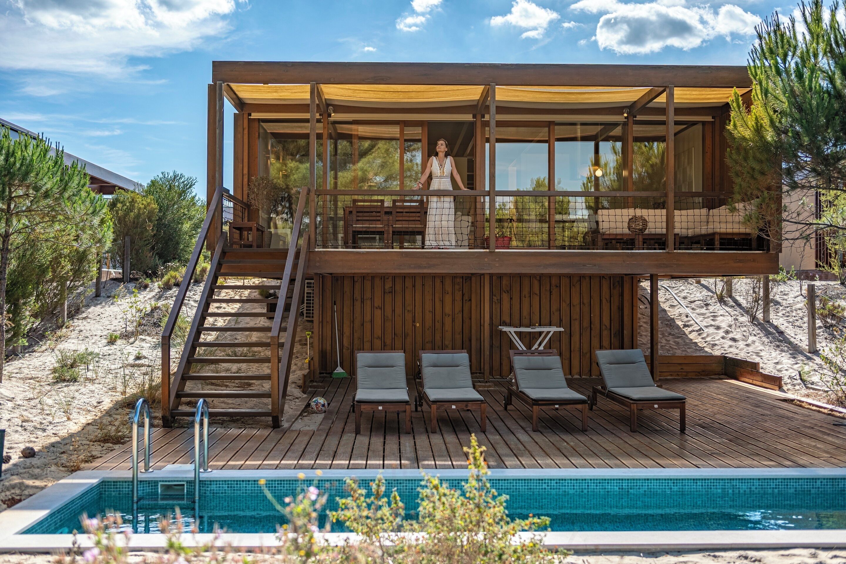 Una casa a due piani in legno con un balcone, una piscina e sedie a sdraio.