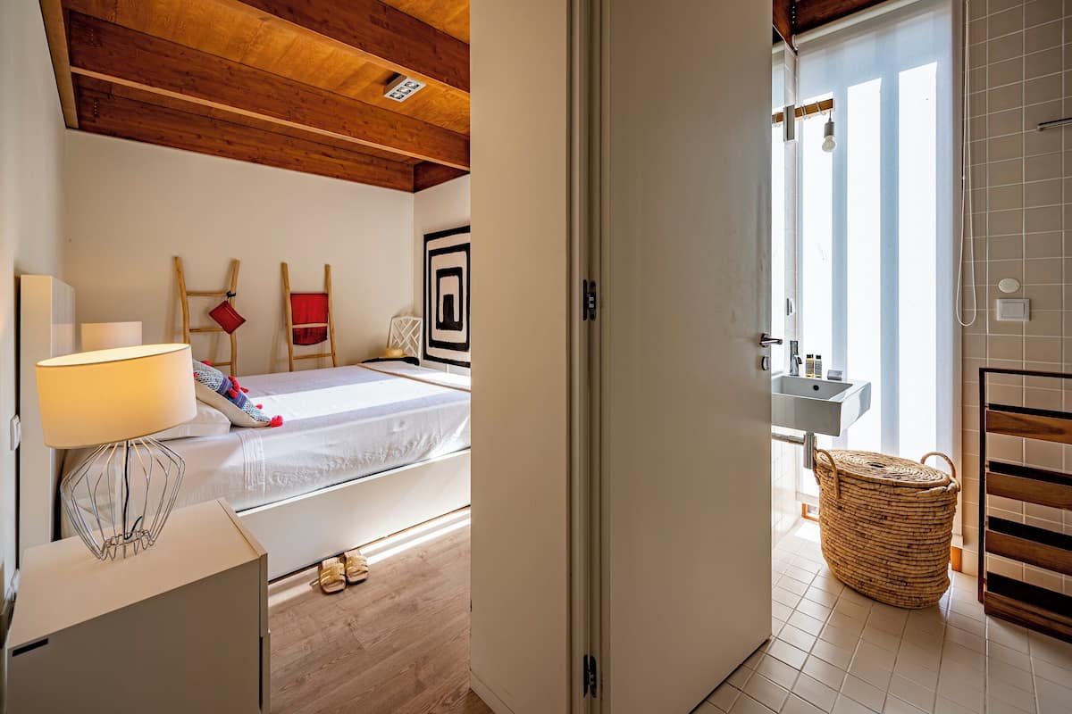 Un dormitorio con cama, lámpara de noche y techo de madera.