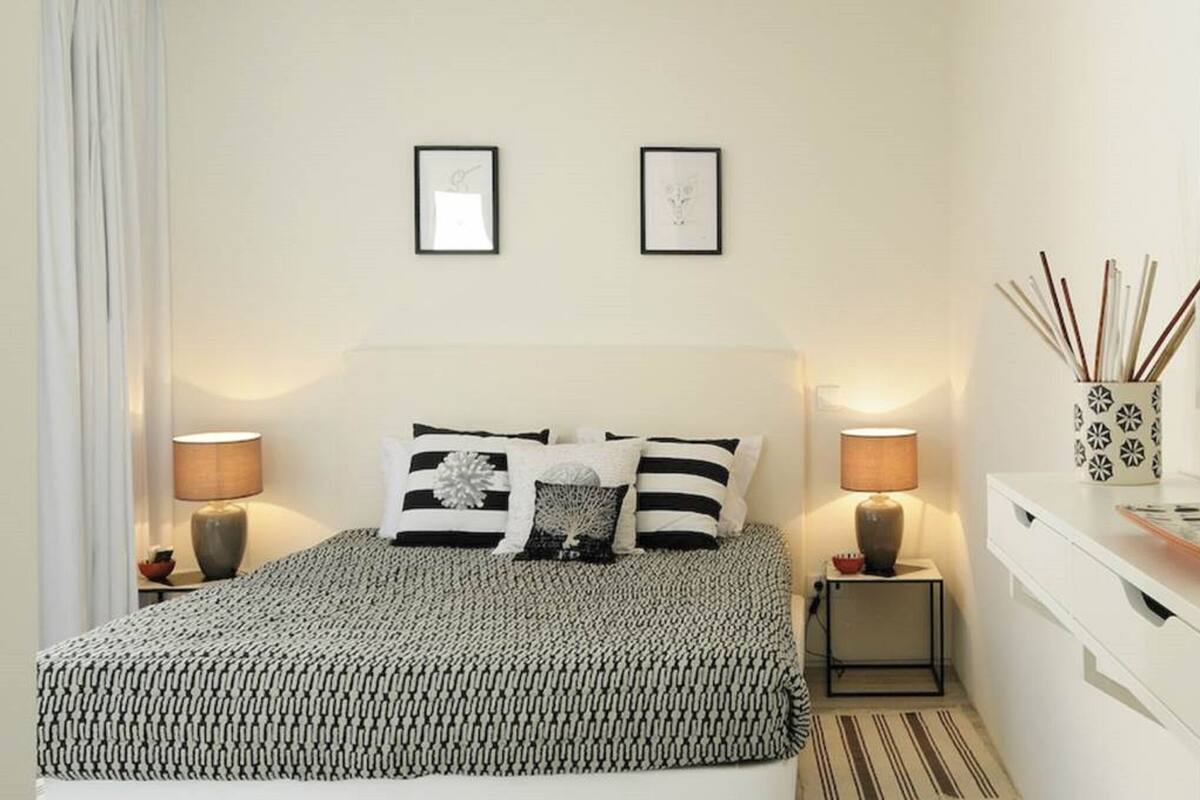 Un dormitorio con cama, mesitas de noche, cómoda, espejo y decoración en la pared.