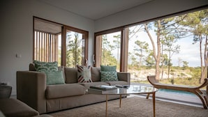 A modern living room with a sofa, coffee table, and a view of a natural landscape through large windows. - Pestana Tróia (Grandola)