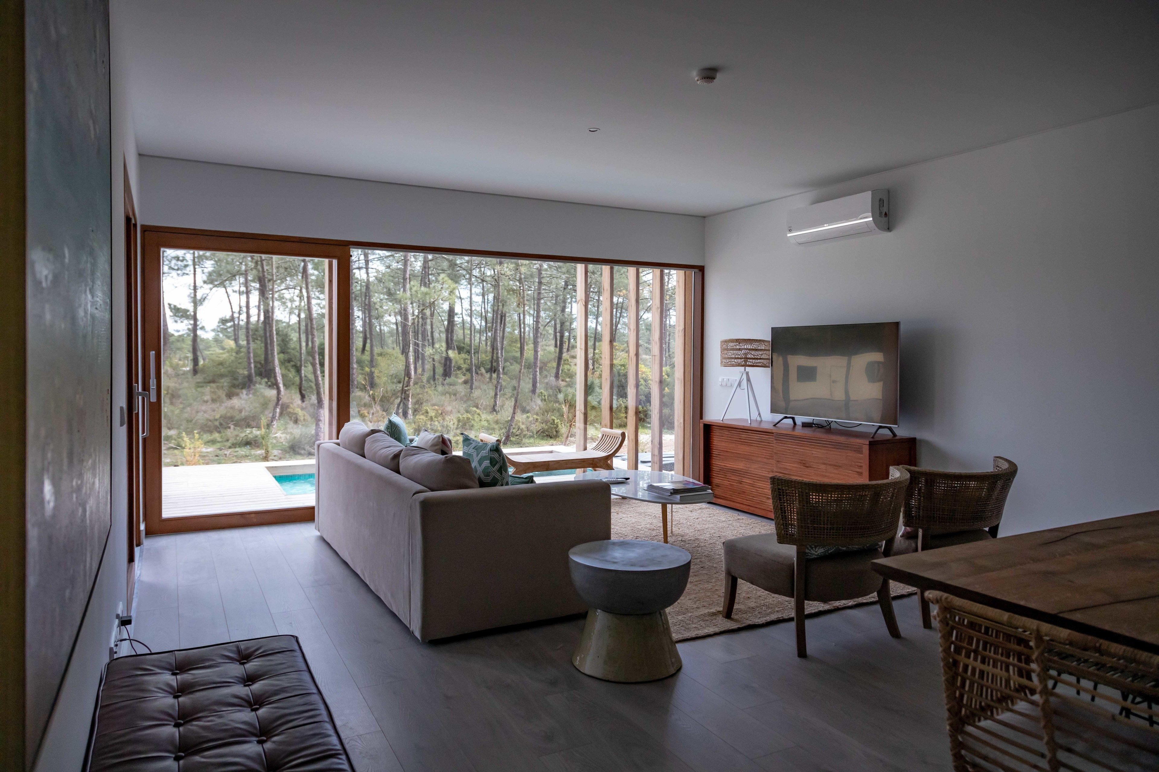 Una sala de estar moderna con un gran ventanal corredizo que da a una piscina, un sofá, una mesa de comedor con sillas y un televisor.
