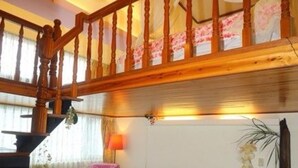 A spacious living area with a red sofa, a wooden staircase, and a view of the outdoors. - Jiufen Jiudaokou B&B (New Taipei City)
