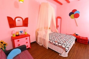Un dormitorio rosa con cama a dosel, mesita de noche roja con cajones y una mesilla con lámpara.