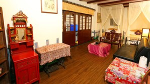 A traditional room with a wooden floor, a red cabinet, a table with a floral tablecloth, a sofa, and a bed with a canopy. - Jiufen Jiudaokou B&B (New Taipei City)