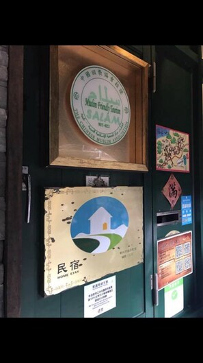 A wall with various signs and decorations, including a framed sign for Muslim Friendly Tourism, a 'Home Stay' sign, and a QR code for a mobile app. - Jiufen Jiudaokou B&B (New Taipei City)