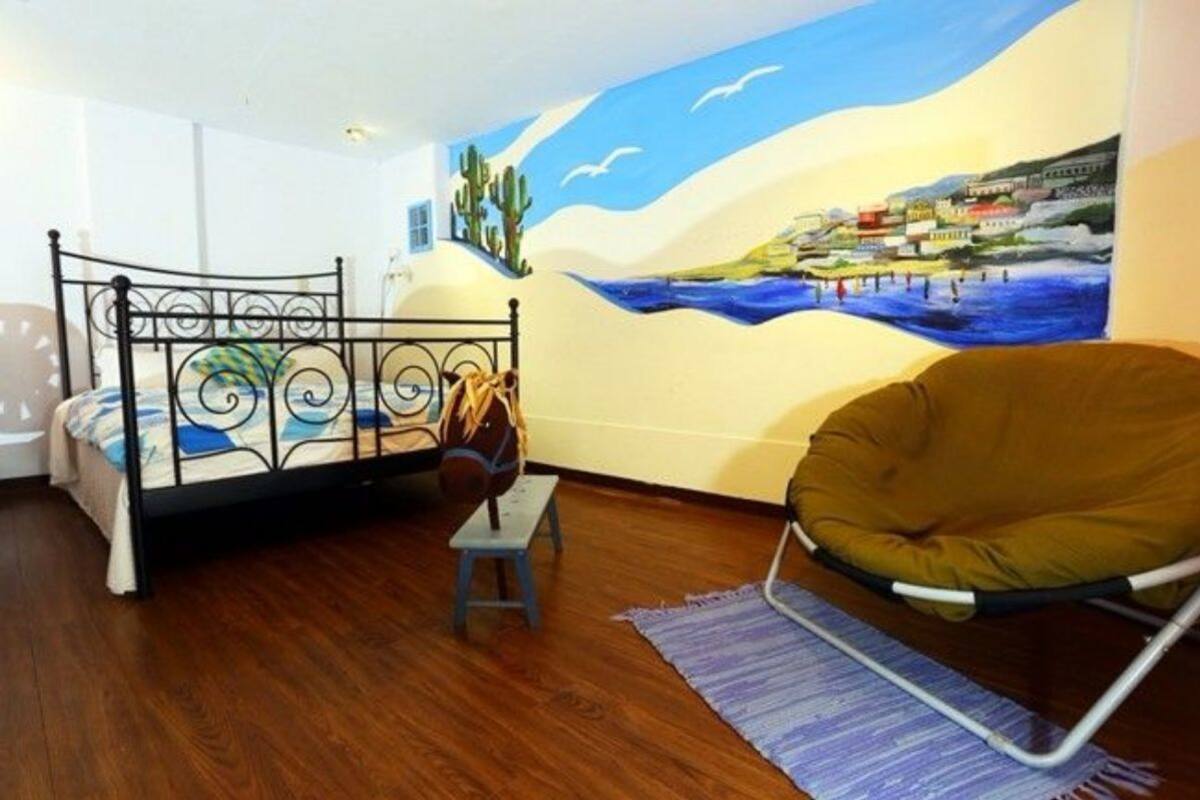 A room with a bed, a chair, a small stool, and a mural on the wall.