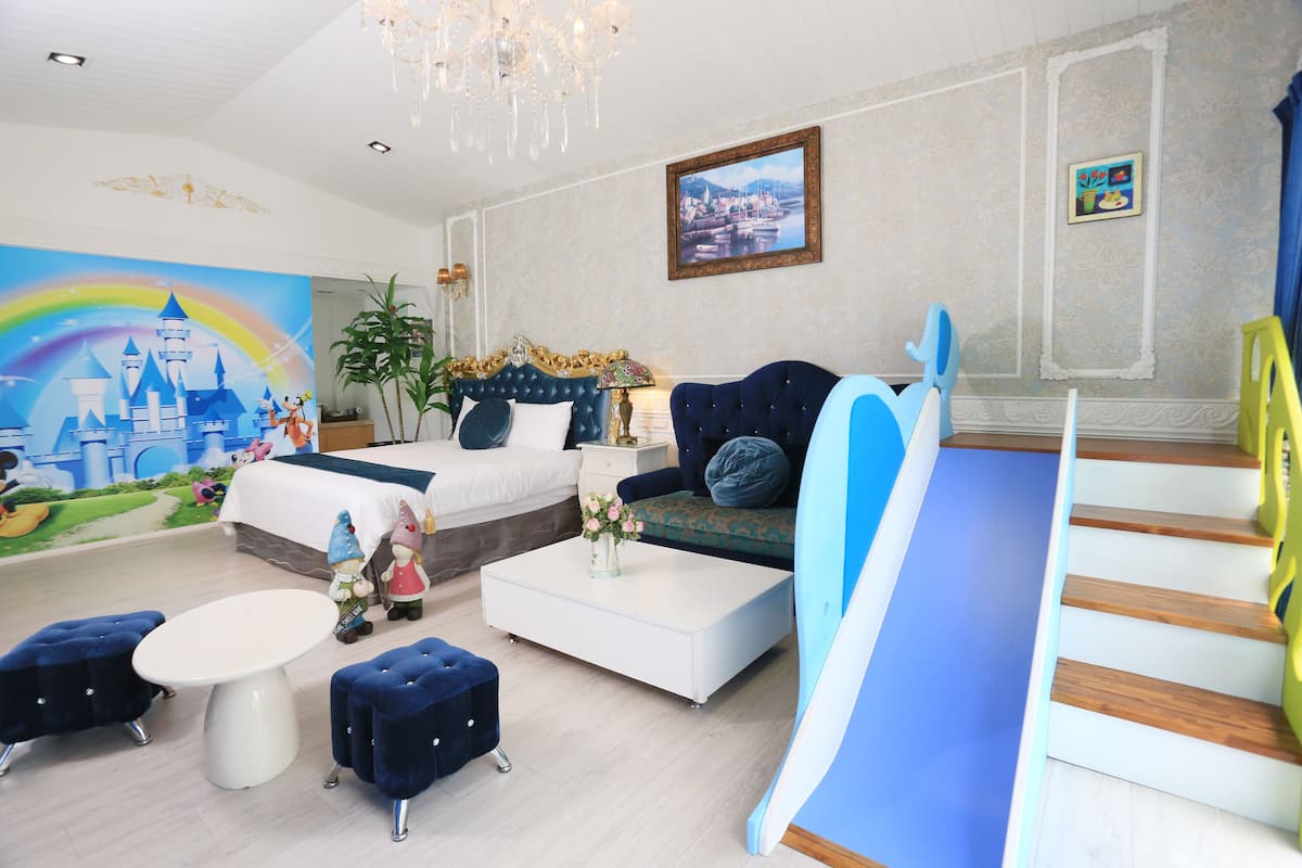 A hotel room with a bed, a sofa, a coffee table, a dining table, a staircase, and a mural of a castle.