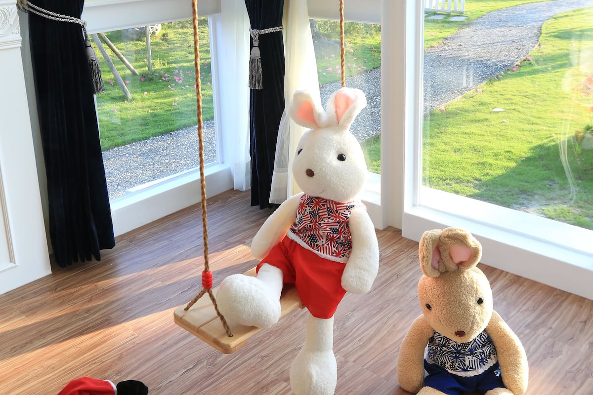 A room with a large window, a swing hanging from the ceiling, and two plush toys on the floor.