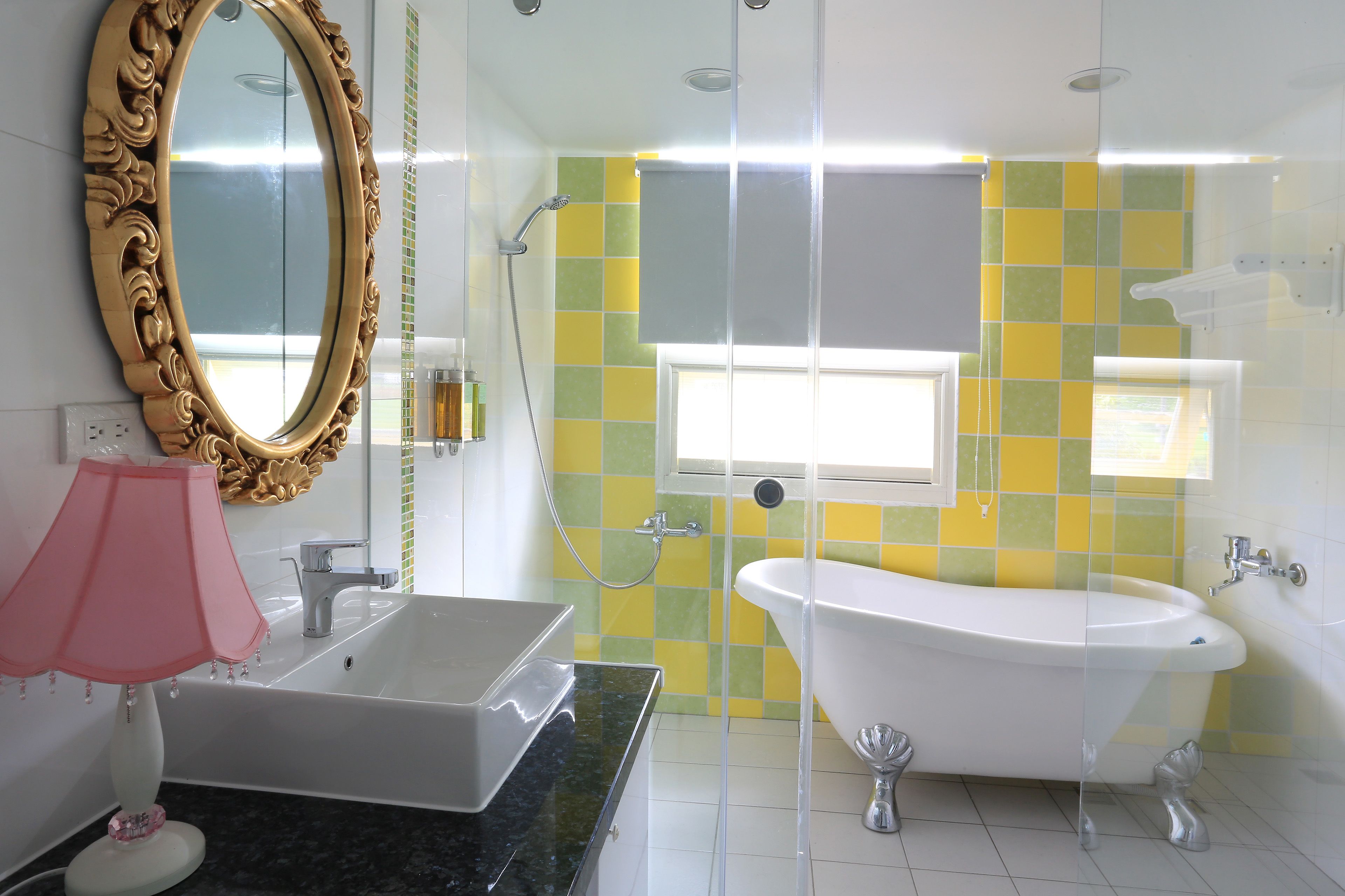 A bathroom with a white sink, a large mirror, a bathtub, and a window with yellow and green tiles.