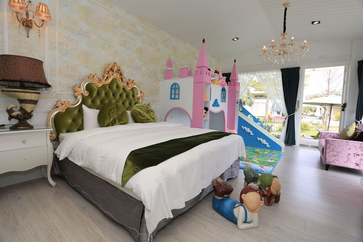 A bedroom with a large bed, a castle play area, and a chandelier.