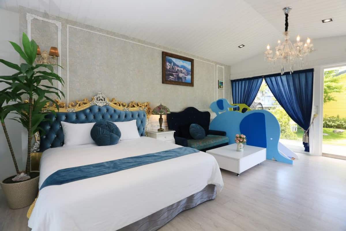 A bedroom with a large bed, a nightstand, a potted plant, a chair, and a view of the outdoors.