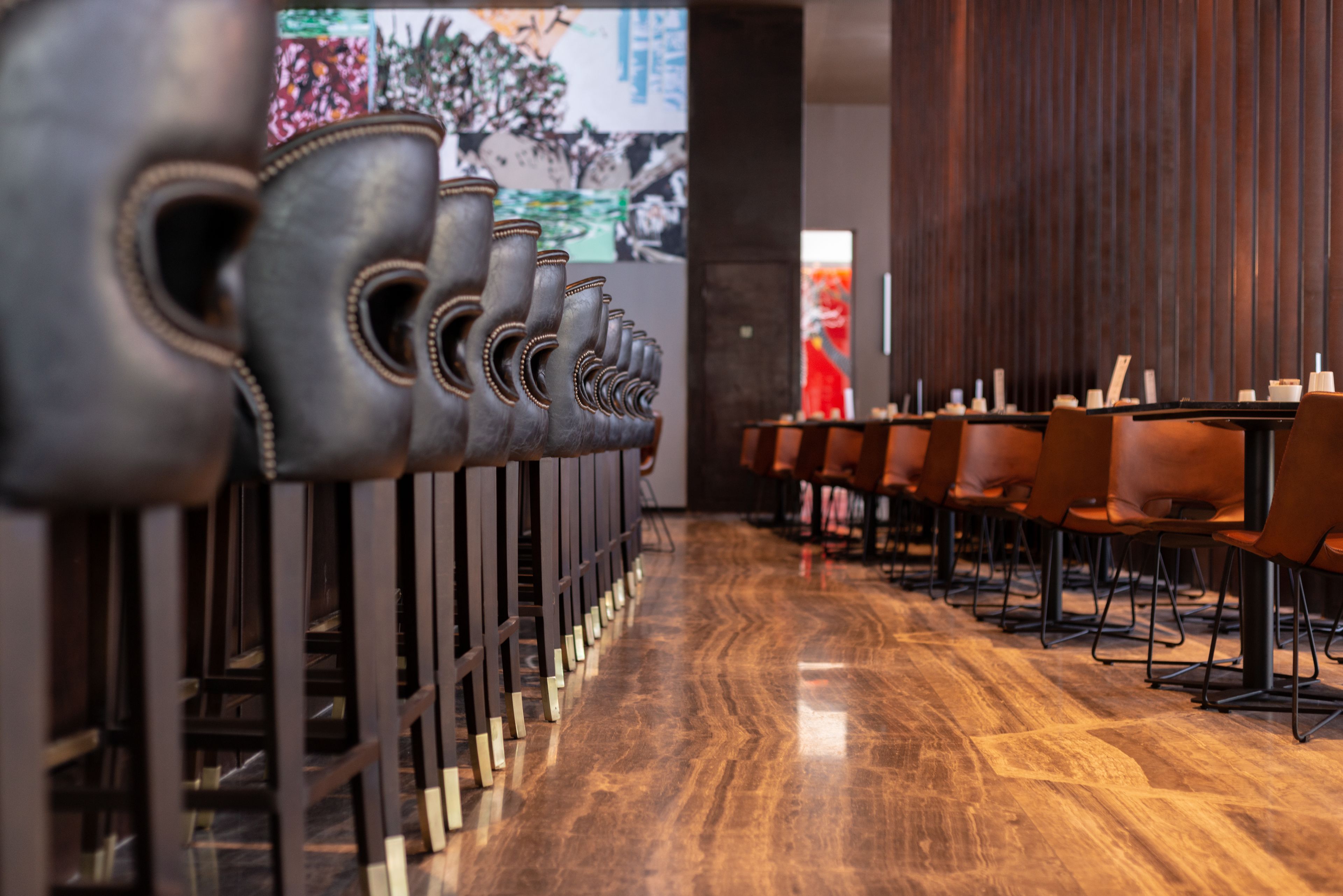 A row of chairs with a unique design, a polished wooden floor, and a large screen displaying artwork in the background.