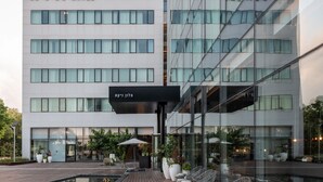 A modern NYX Hotel with a glass facade, outdoor seating area, and a well-maintained garden. - NYX Herzliya (Herzliya)