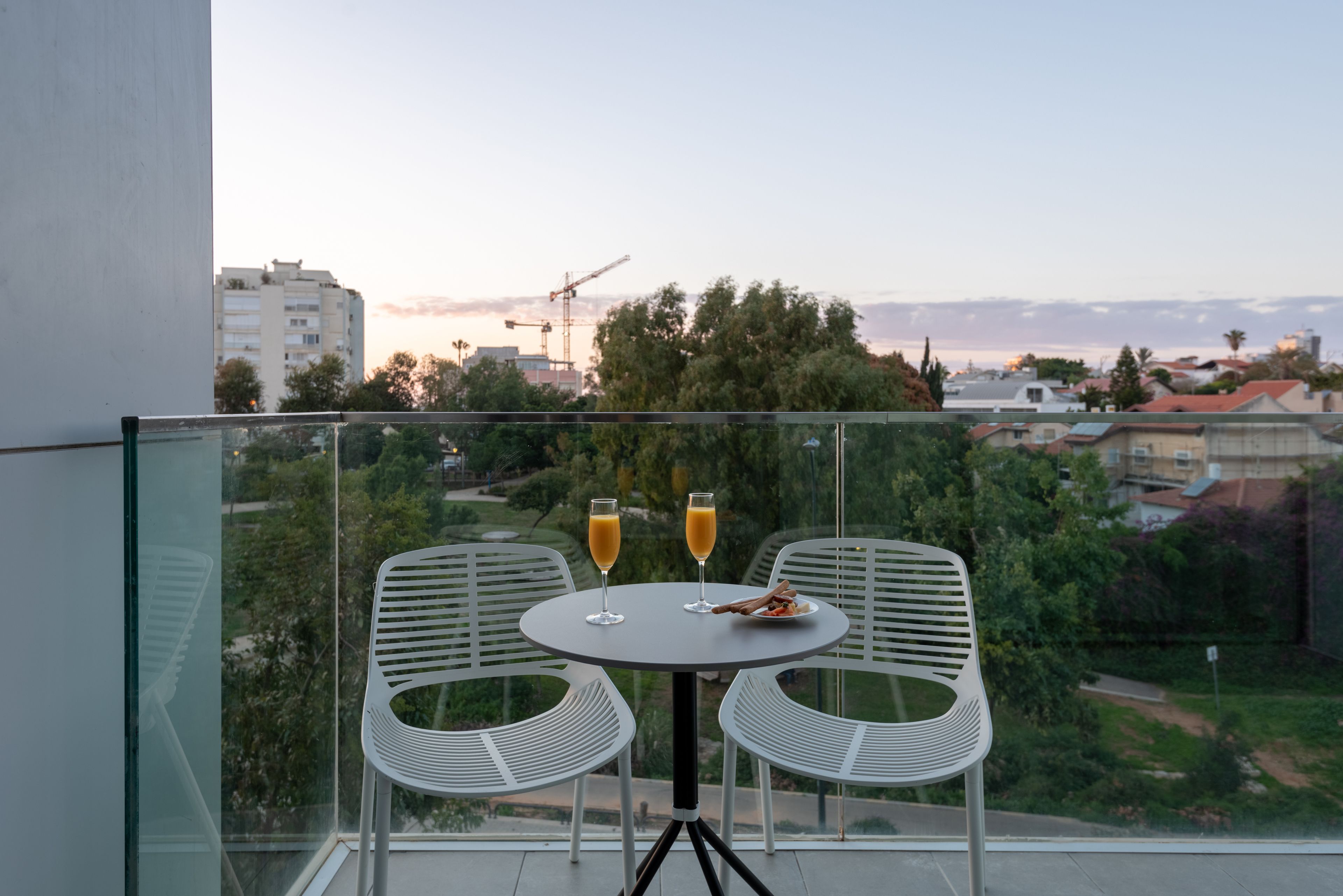 A balcony with a table and two chairs, overlooking a cityscape with buildings and trees.