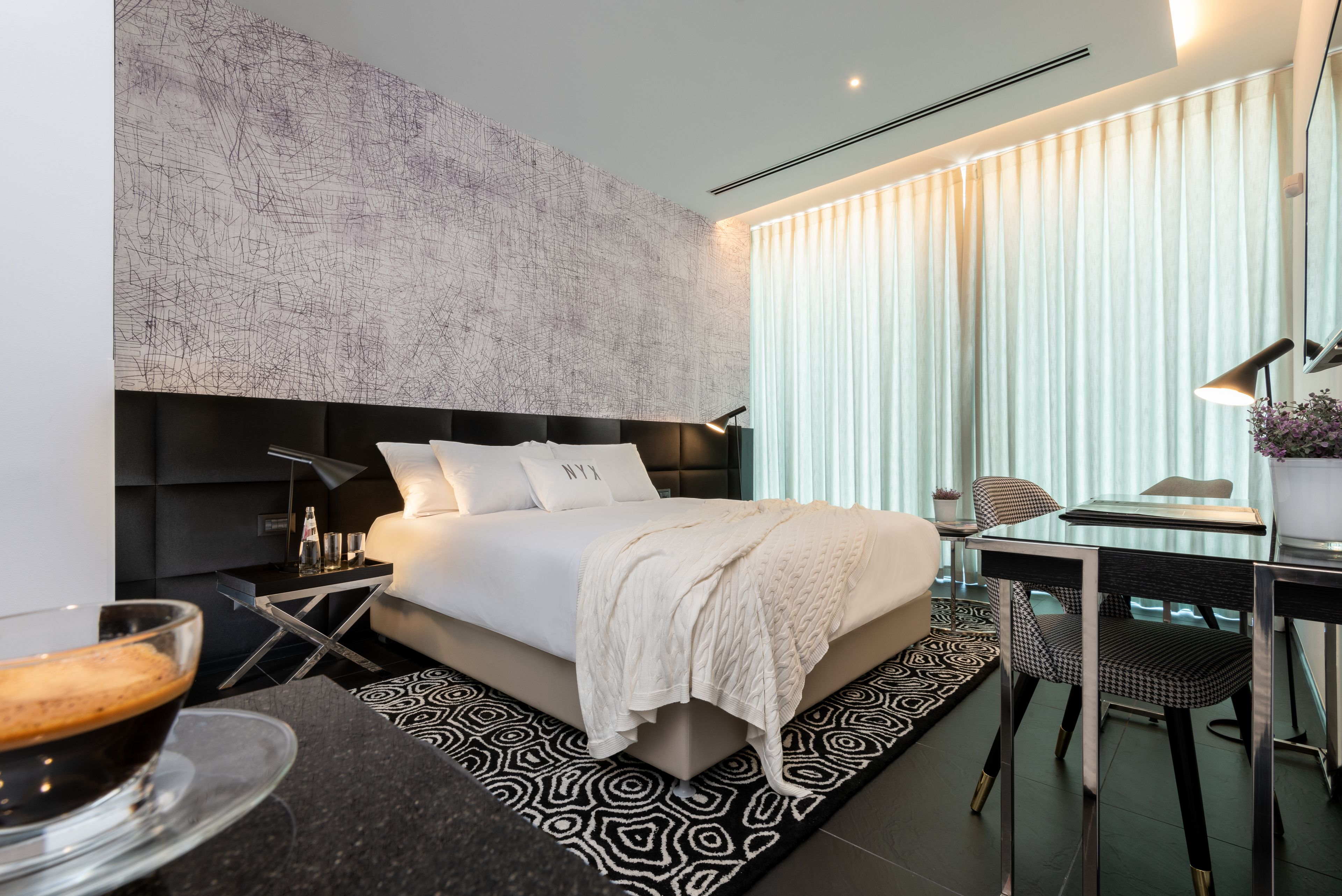 A modern bedroom with a large bed, a bedside table with a lamp, and a glass coffee table.