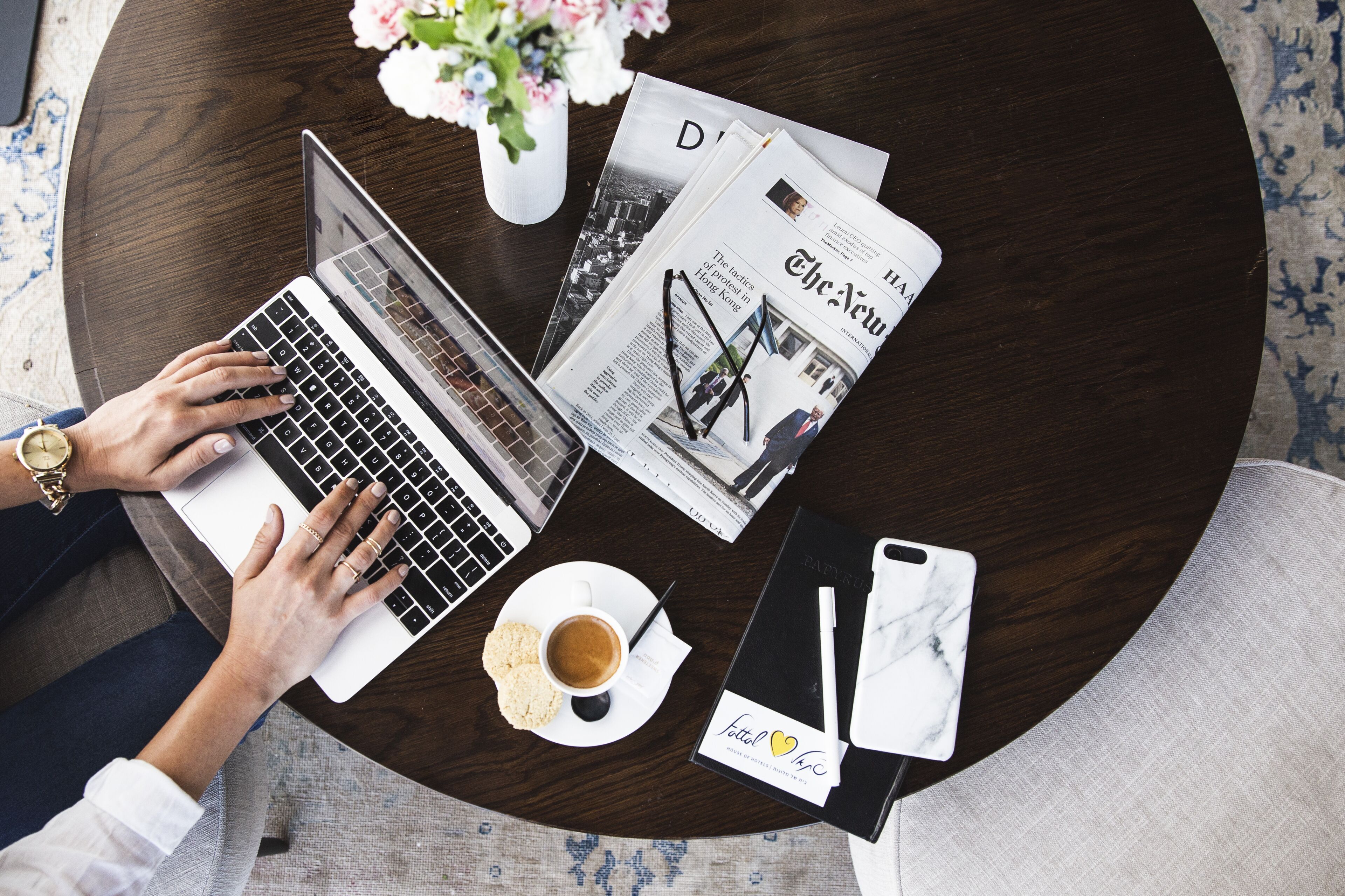 A laptop on a round table with a newspaper, a cup of coffee, and a smartphone.