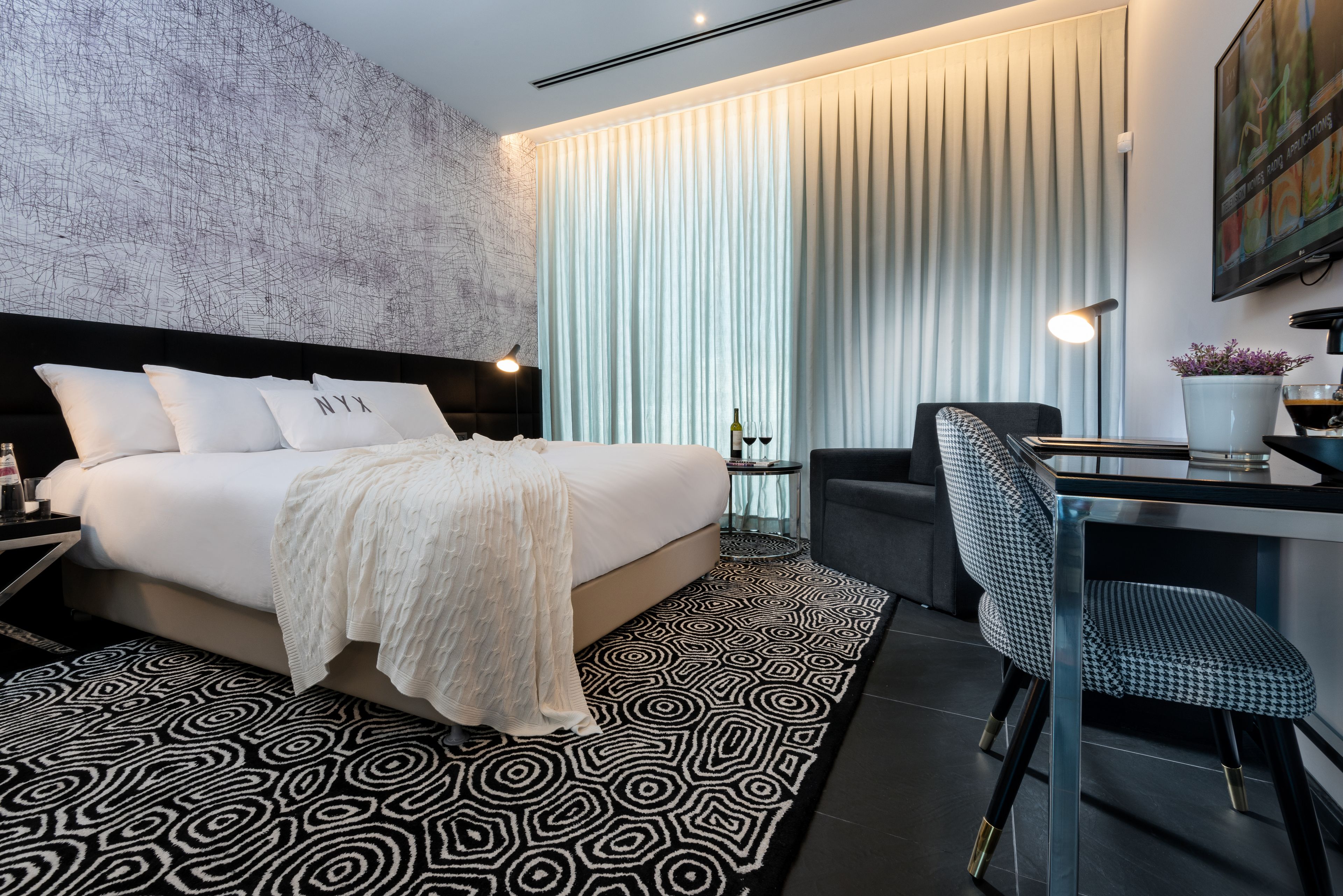 A modern hotel room with a large bed, a desk, and a chair.