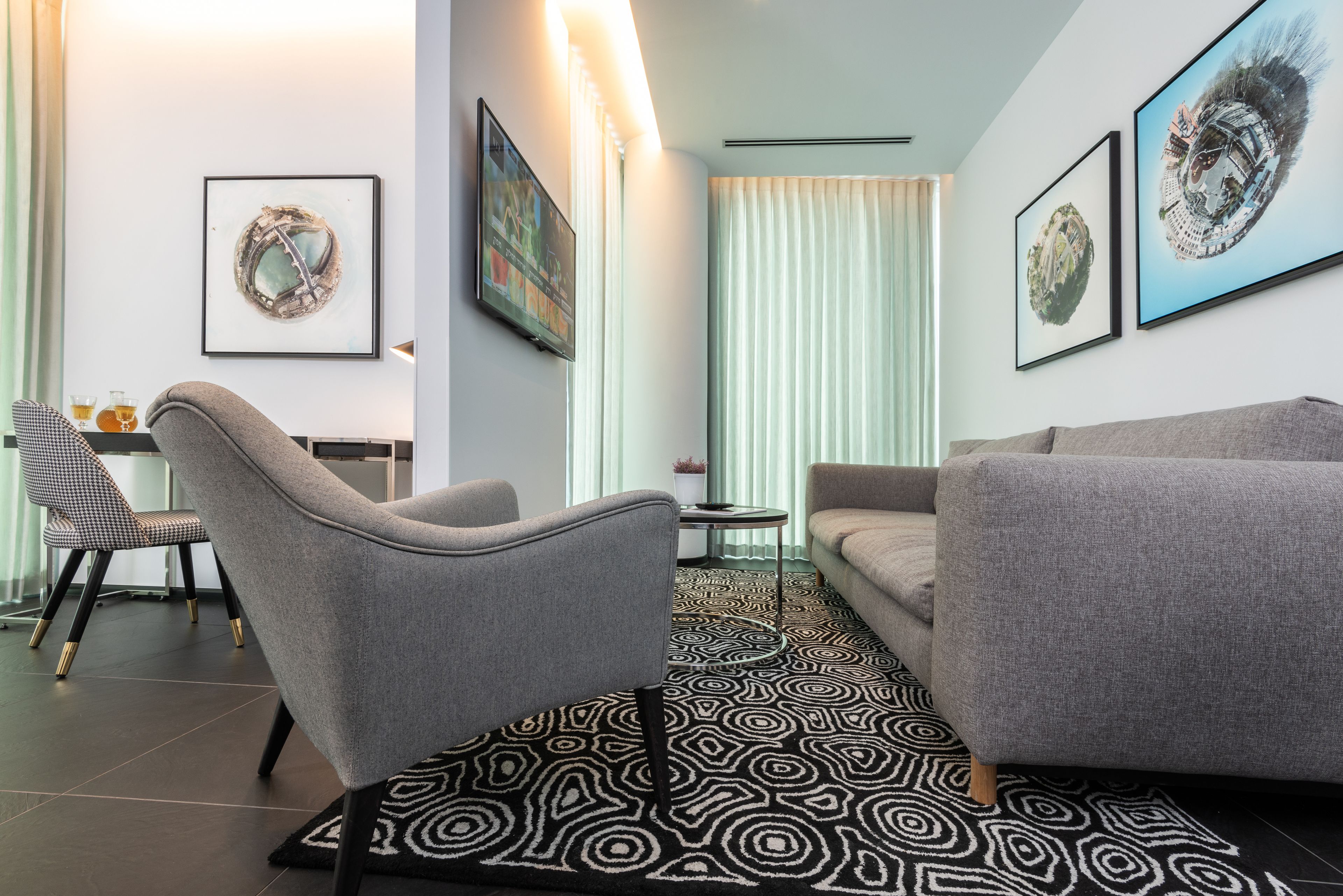 A modern living room with a grey sofa, a grey armchair, a patterned rug, and framed artwork on the walls.