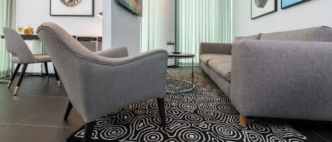 A modern living room with a grey sofa, a grey armchair, a patterned rug, and framed artwork on the walls.