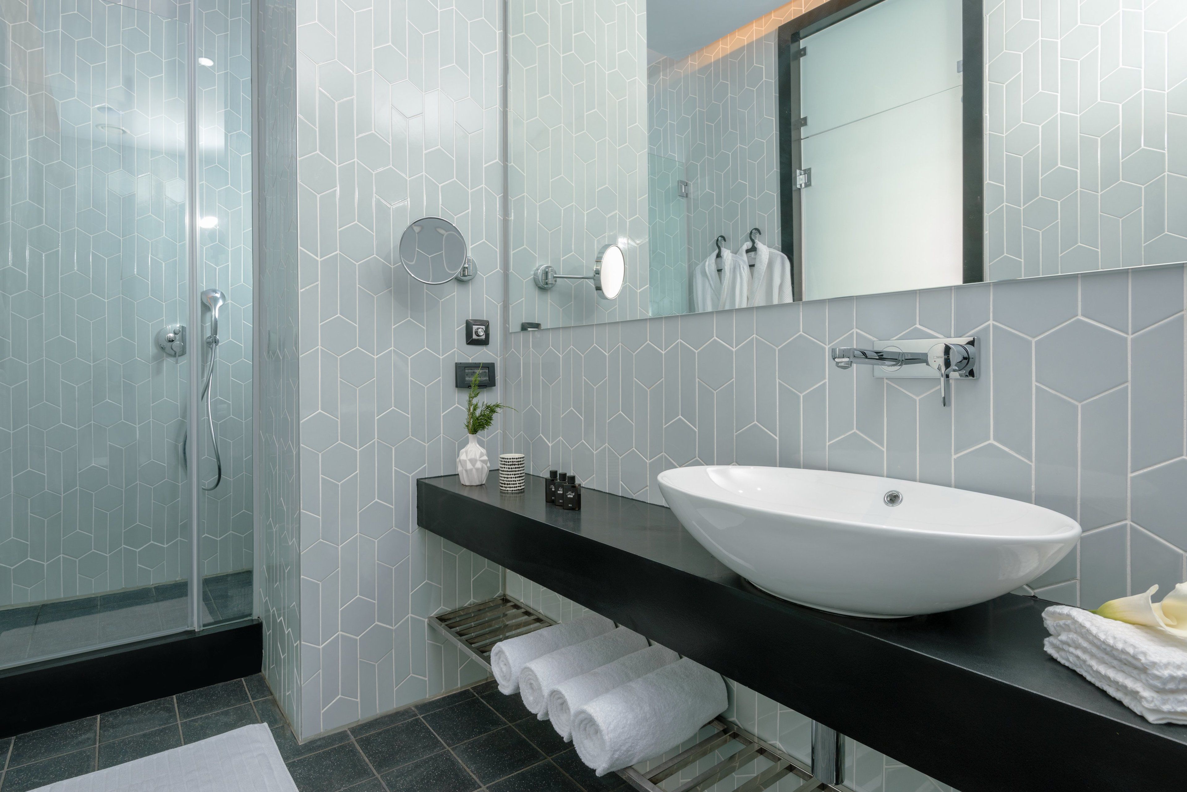 Un baño moderno con ducha de vidrio, un lavamanos grande de color blanco y una encimera negra.