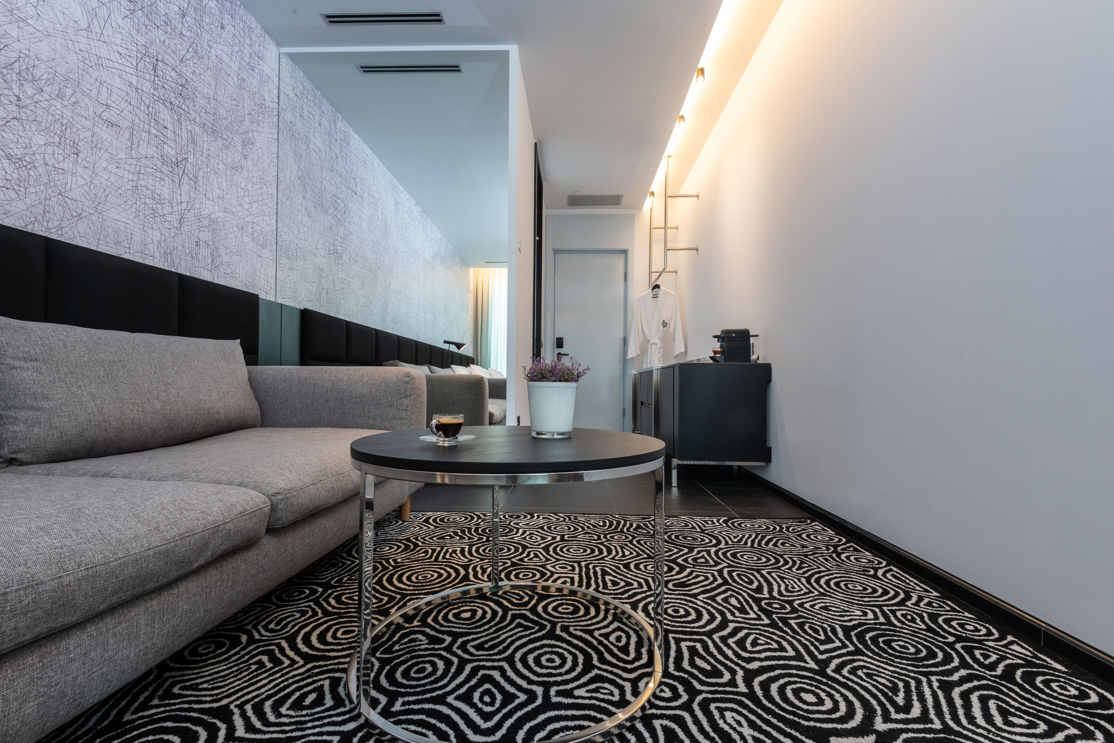A modern hotel room with a grey sofa, a round coffee table, and a patterned floor.
