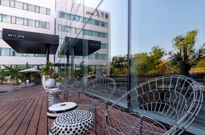 Relax in a stylish outdoor seating area with metal chairs and round tables, surrounded by trees and a clear sky.