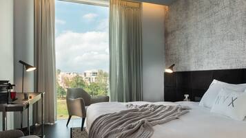 Habitación de hotel con una cama grande, un escritorio con lámpara, una silla y vistas al exterior.