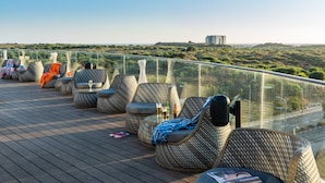 A rooftop terrace with wicker lounge chairs, a glass railing, and a view of a hilly landscape. - NYX Herzliya (Herzliya)