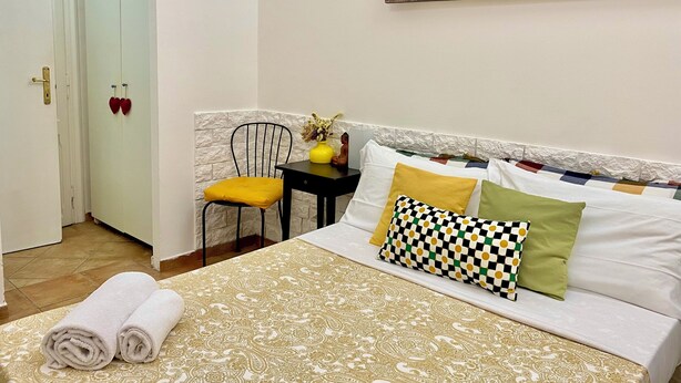 A hotel room with a bed, a chair, a painting of the Colosseum, and a white door. - Domus Romana B & B (Rome)