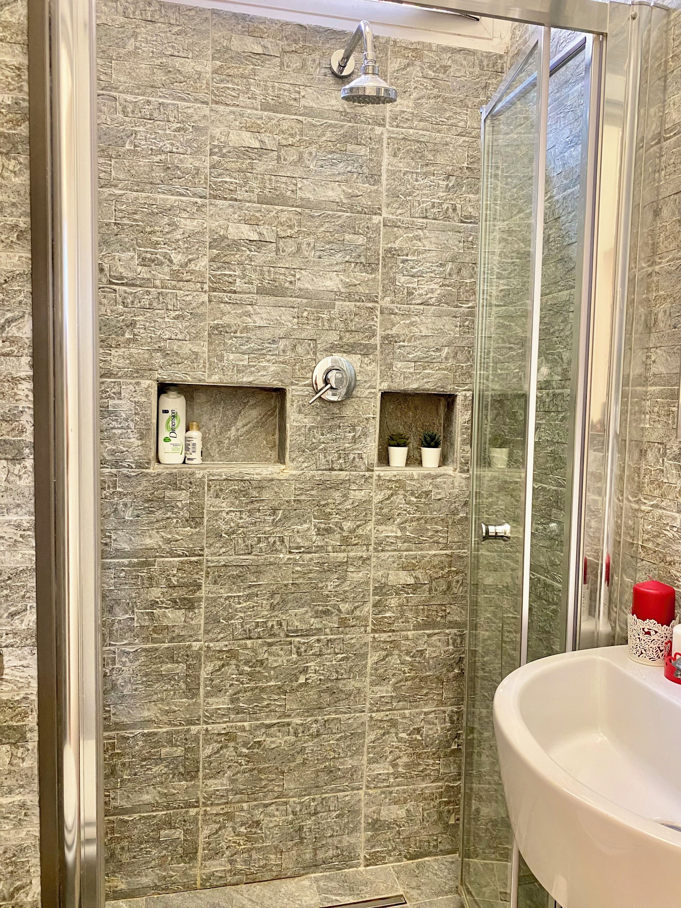 A modern bathroom with a shower enclosure, a glass door, and a sink with toiletries.